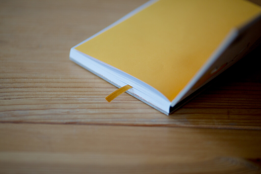 Yellow hardcover book with white spine on wooden surface, showing binding detail.