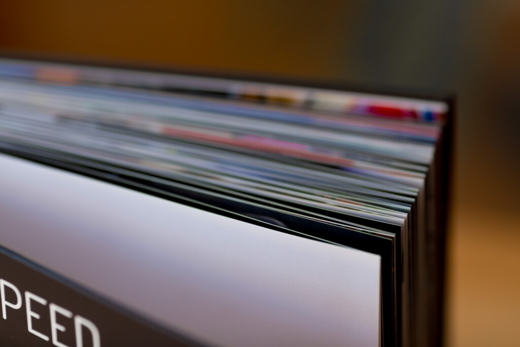 Stack of printed photo albums fanned open, showing coloured pages and black spines.