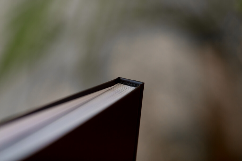 Close-up of a book spine with black binding and white pages visible against a blurred background.