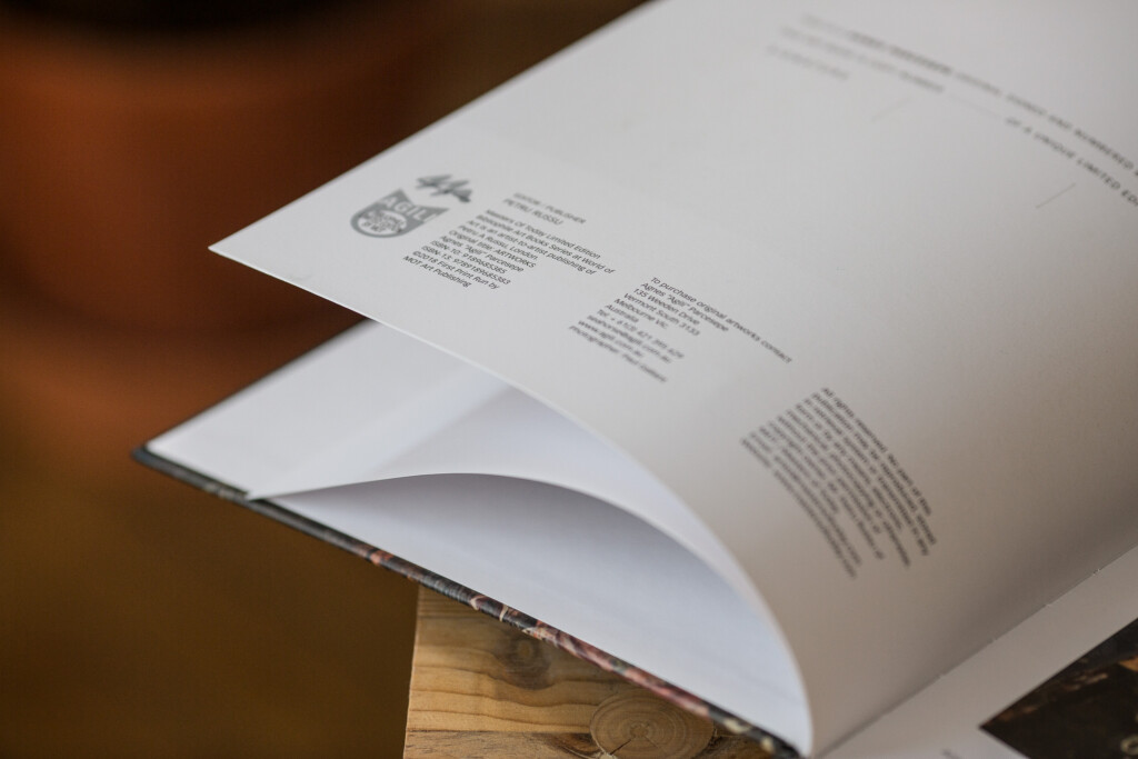 Hardcover book open to show interior pages with text and logo, displayed at an angle on a wooden surface.