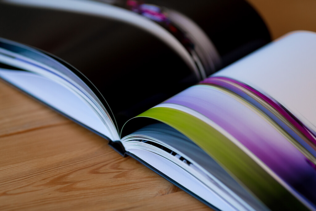 Open photo album with colourful gradient page edges fanned out on wooden surface, showing sewn binding and white interior