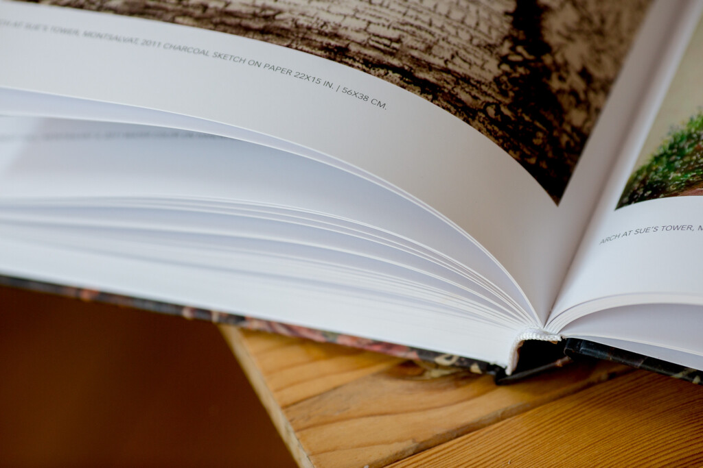 Hardcover book with open spread displaying blank pages, resting on wooden surface with bark textured cover visible.