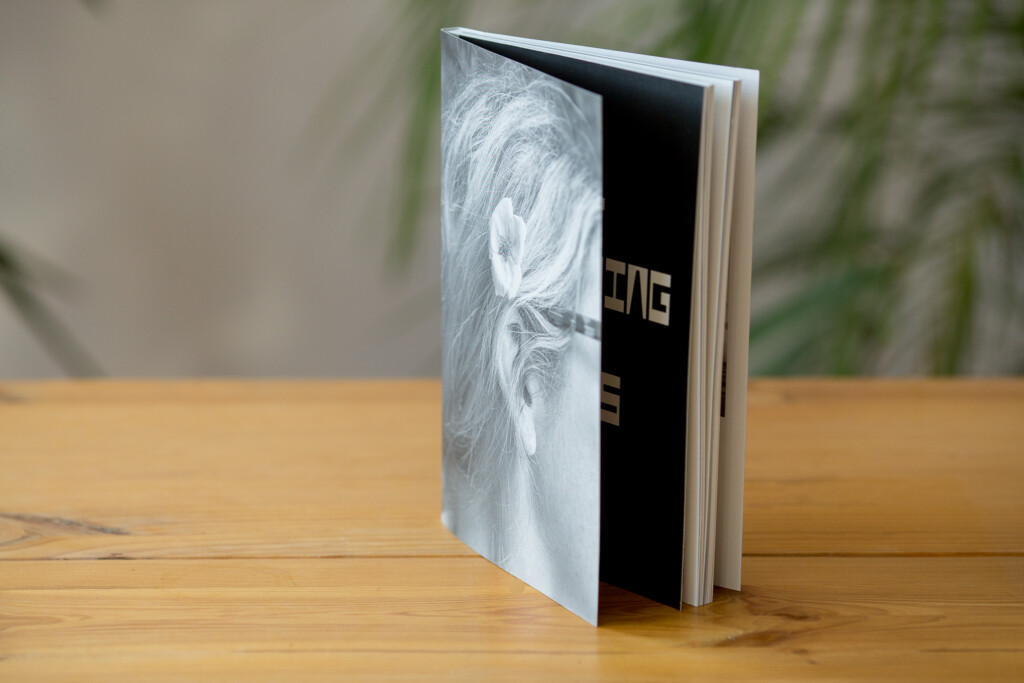 Softcover book with Swiss binding and linen spine, open to show interior pages with text against wooden surface.