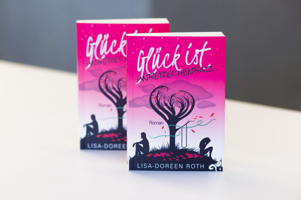 Two copies of softcover book "Glück ist" by Lisa-Doreen Roth with pink gradient cover and silhouetted figures beneath a