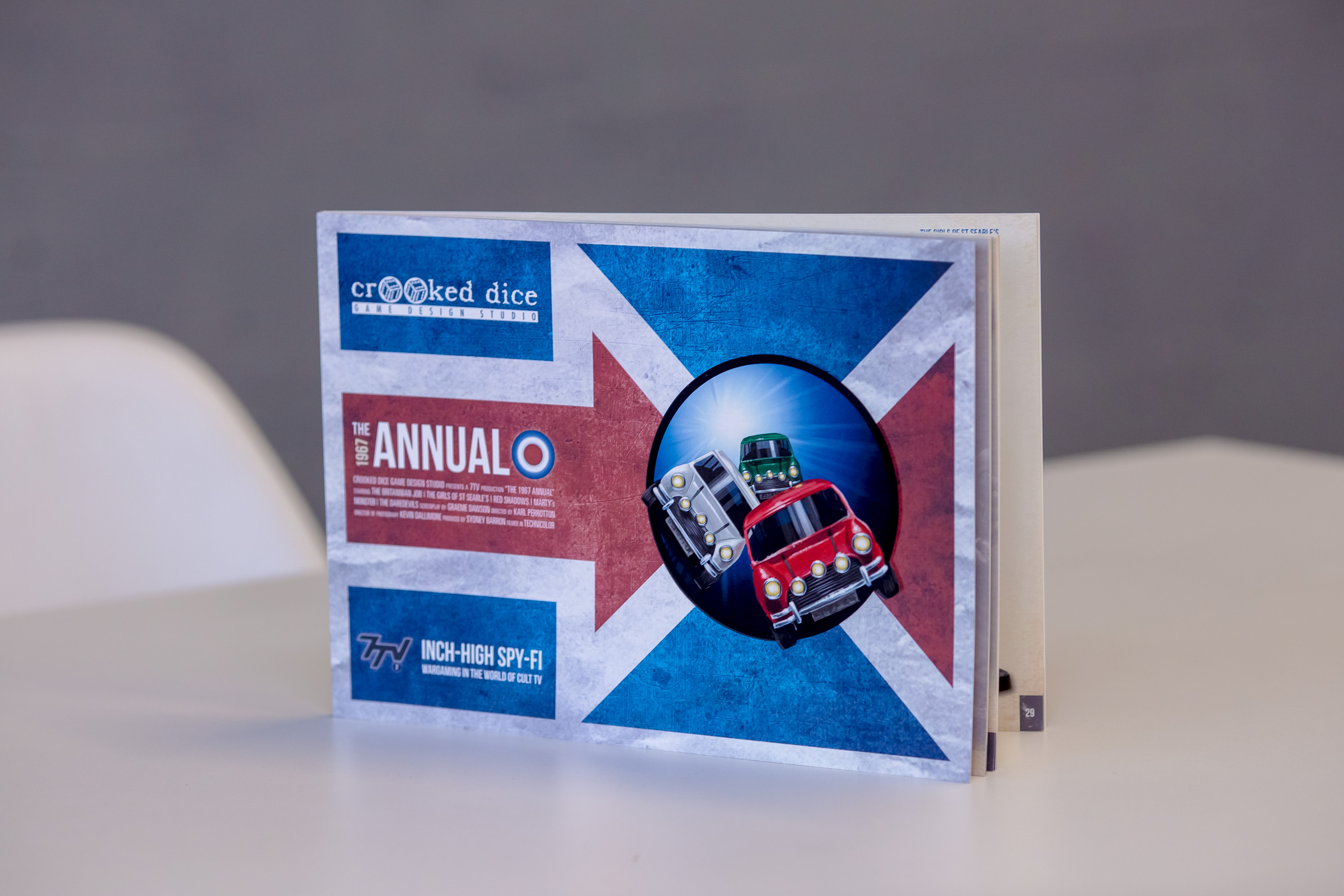 Hardcover game manual with Union Jack design, red bus illustration and blue circular element on cover, displayed at an angle.