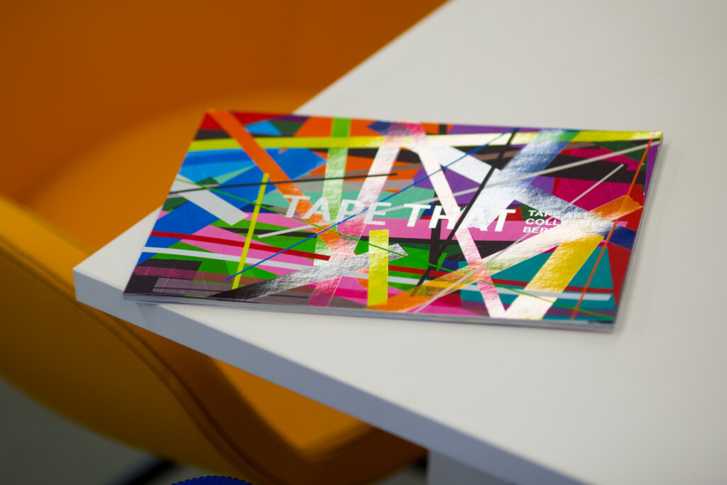 Hardcover art catalogue with multicoloured geometric design and white text on cover, displayed at an angle on white surface.