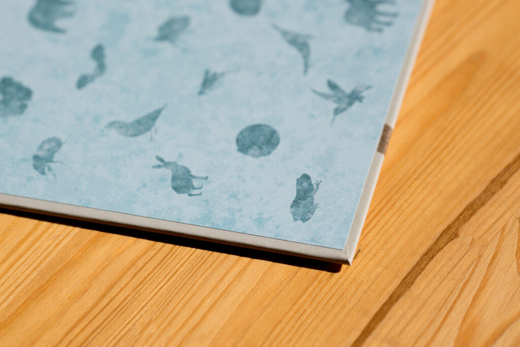 Hardcover cookery book with blue cover featuring illustrated kitchen utensils, displayed on wooden surface.