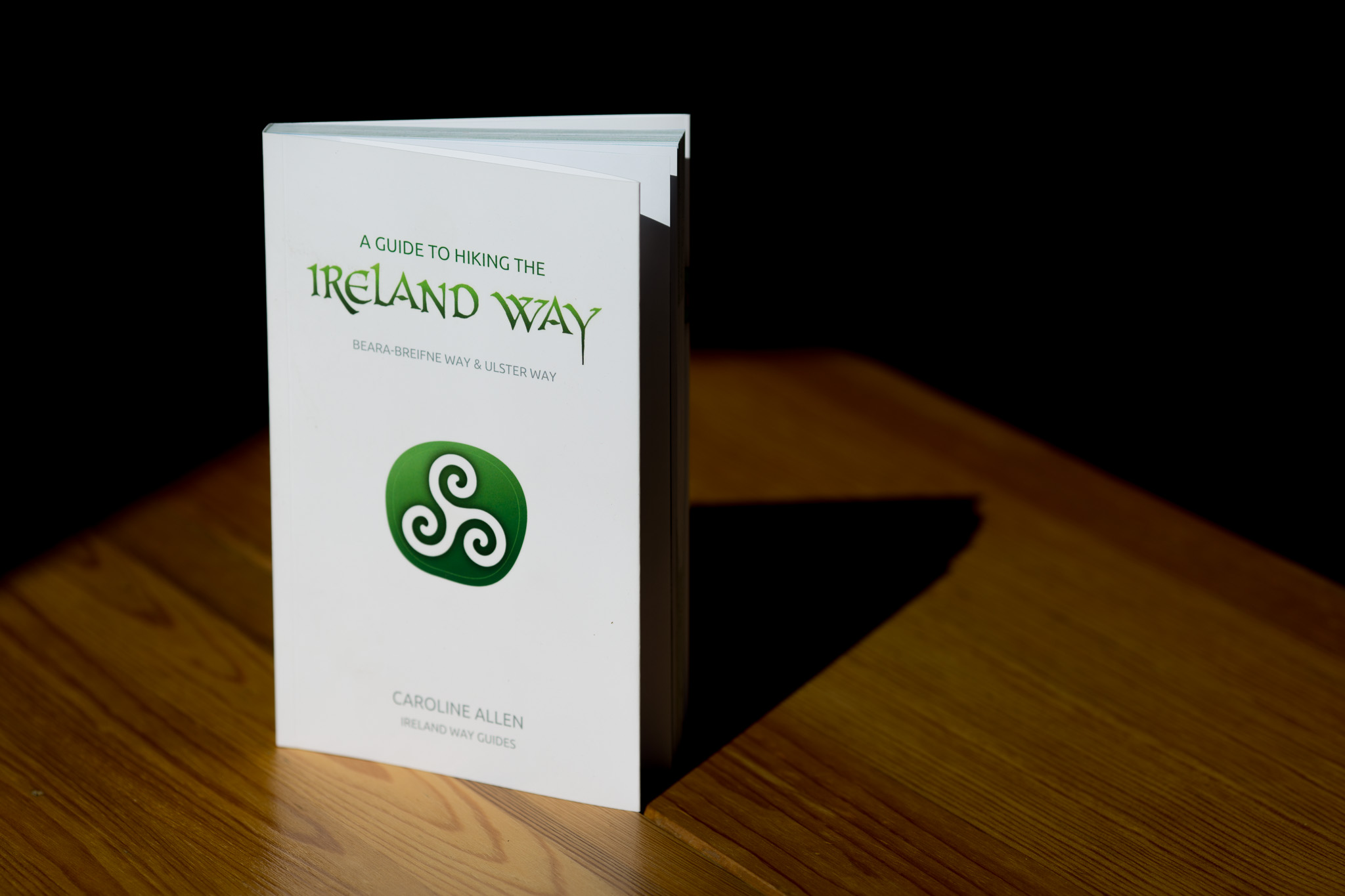 A Guide to Hiking the Ireland Way book with white cover, green spiral symbol and author name Caroline Allen, displayed on