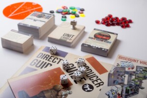 Board game components including rulebooks, dice, coloured tokens, and red beads arranged on a white surface.
