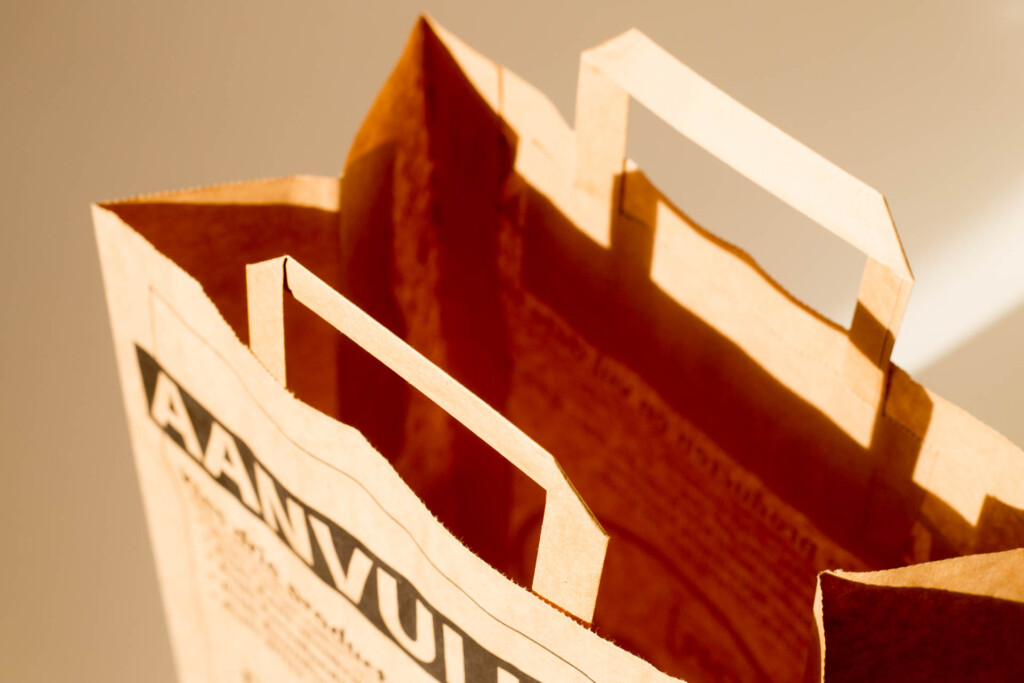 Paper shopping bag with flat handles and red interior, showing the construction of the folded sides and top edge.