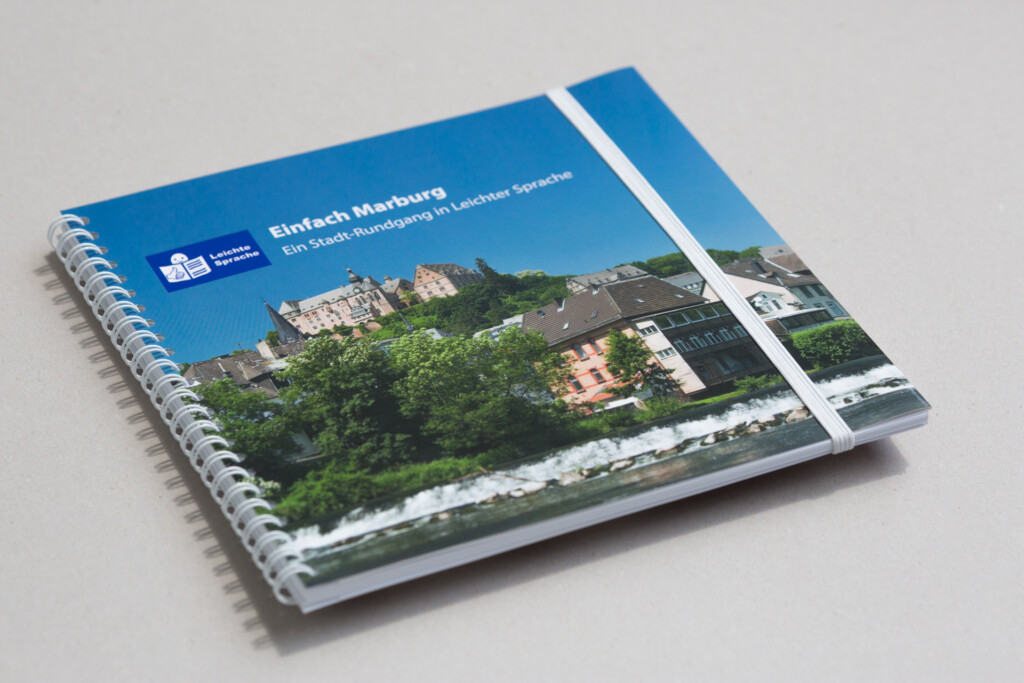 Spiral-bound catalogue with blue cover featuring a castle on a hillside surrounded by green trees and a river below.
