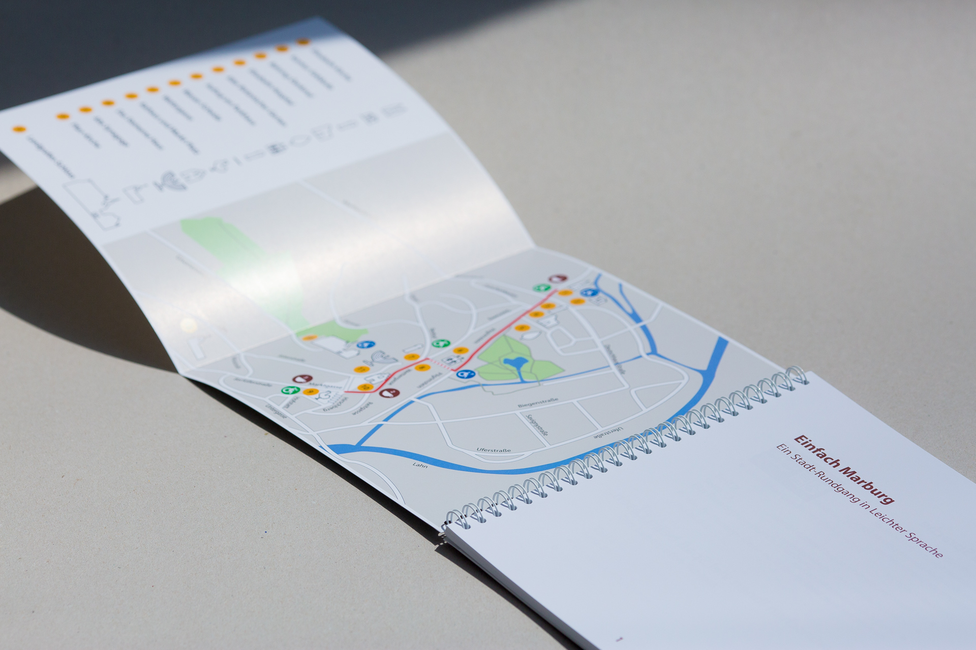 Open spiral-bound notebook fanned to show route map with coloured location pins and blue highlighted path on interior spread.