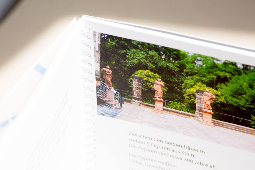 Printed catalogue with wire-o spiral binding, open to show photograph of a terrace with ivy-covered walls and stone urns