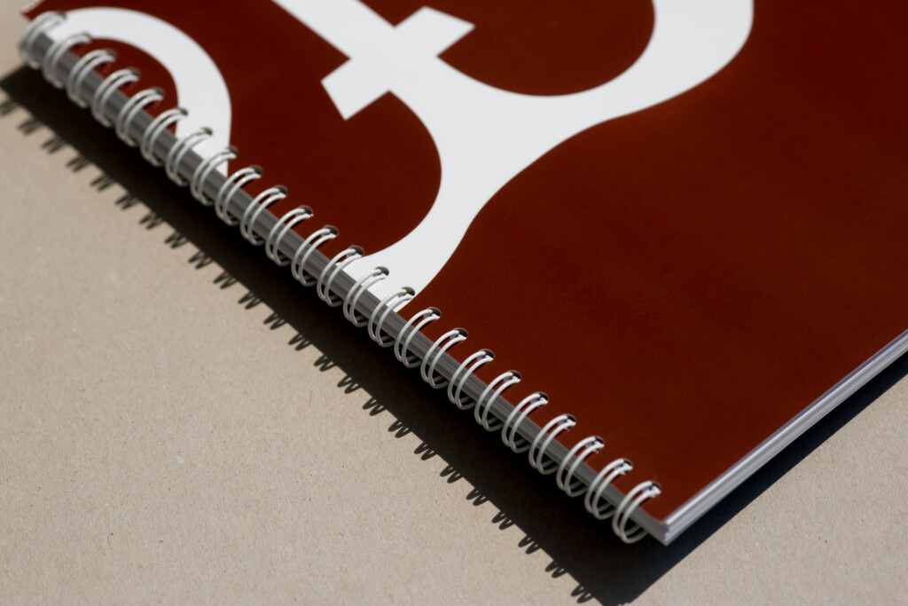 Spiral-bound notebook with burgundy cover featuring white geometric symbol and metal wire-o binding visible along spine edge.