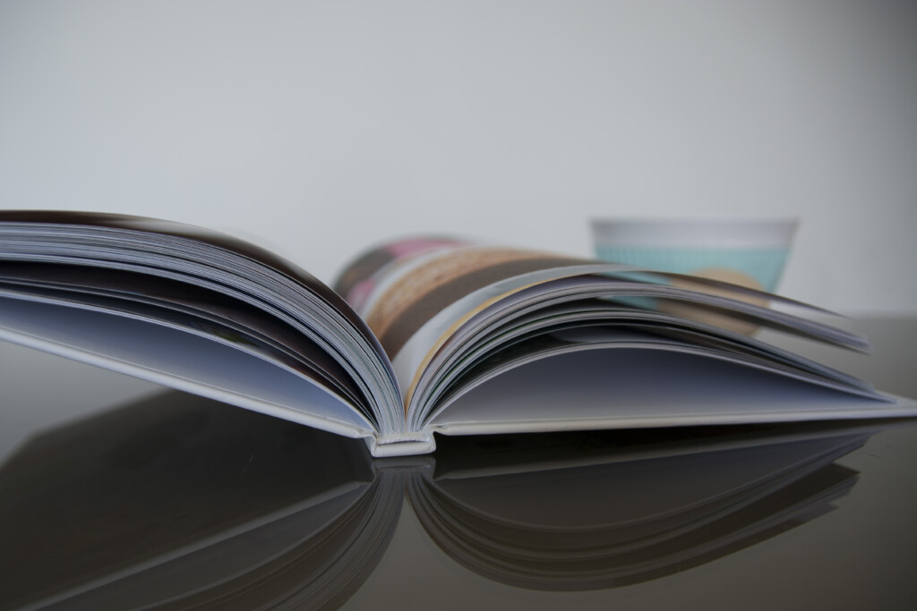 Open hardcover book with glossy pages fanned out, showing colour photography and reflective surface finish.