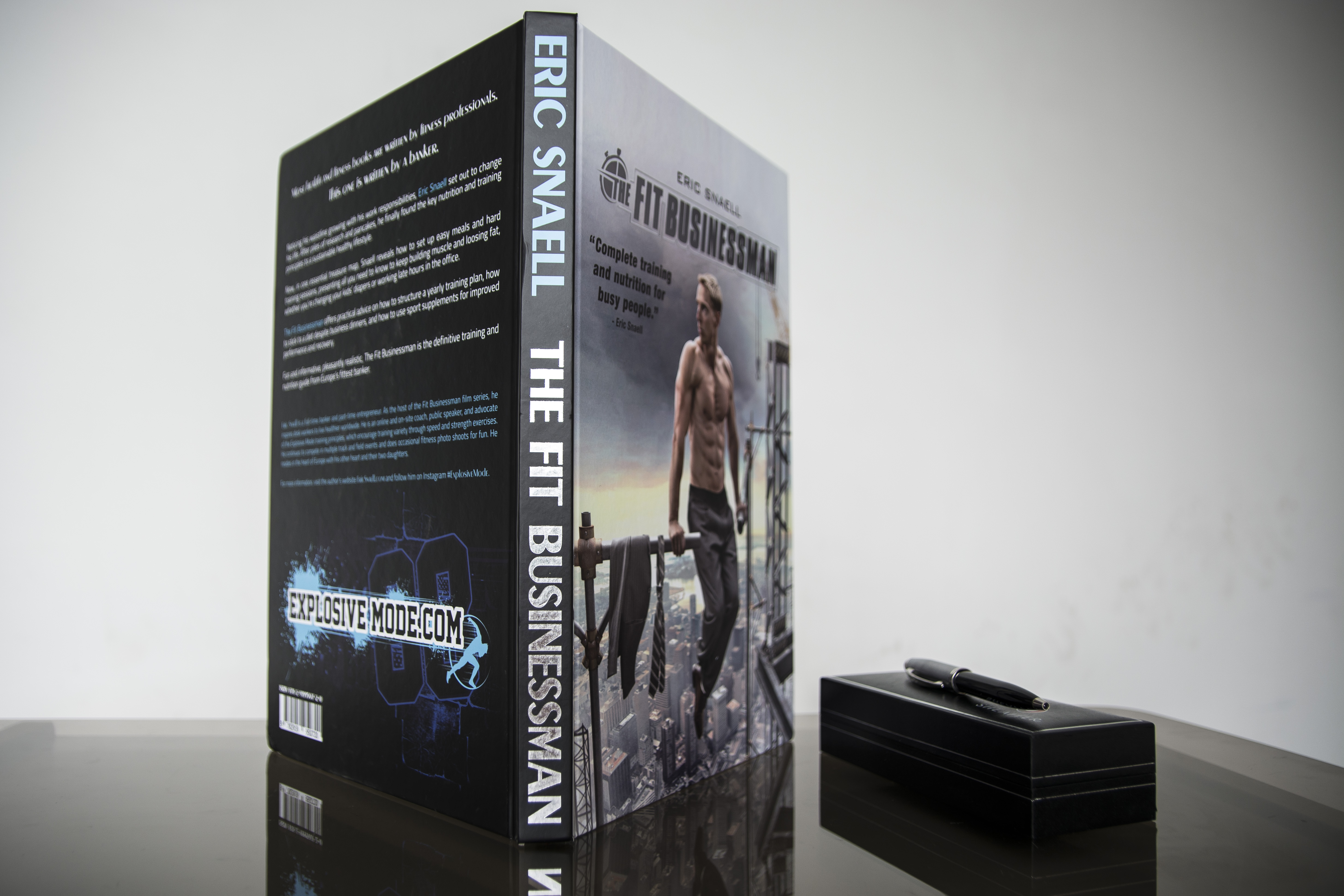 Hardcover book displayed upright next to a black box, showing the spine with title "The Fit Businessman" and front cover