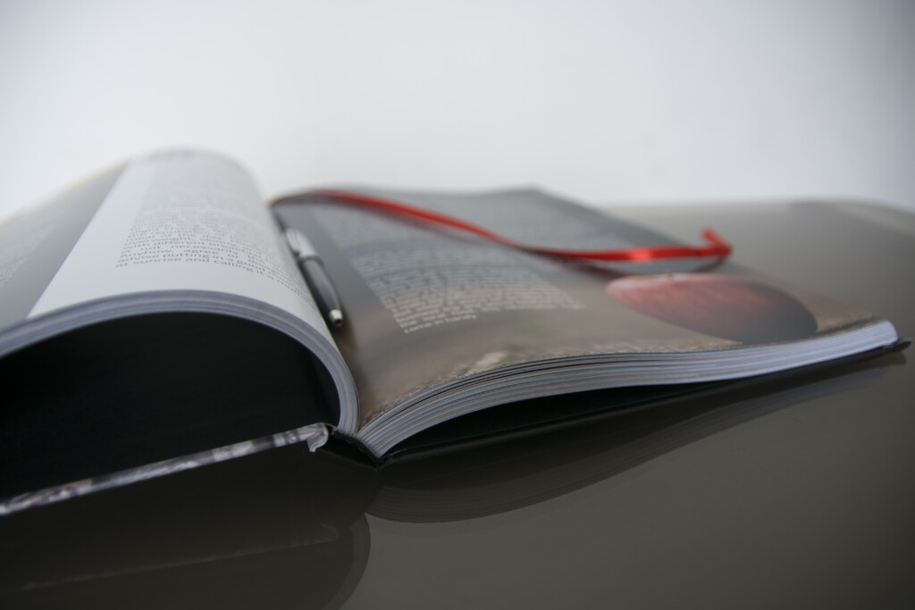 Open hardcover book with red bookmark, displayed on reflective surface.