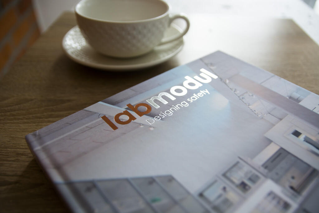 Hardcover catalogue with hot stamping featuring two foil colours, displayed next to a white cup and saucer on a wooden table.