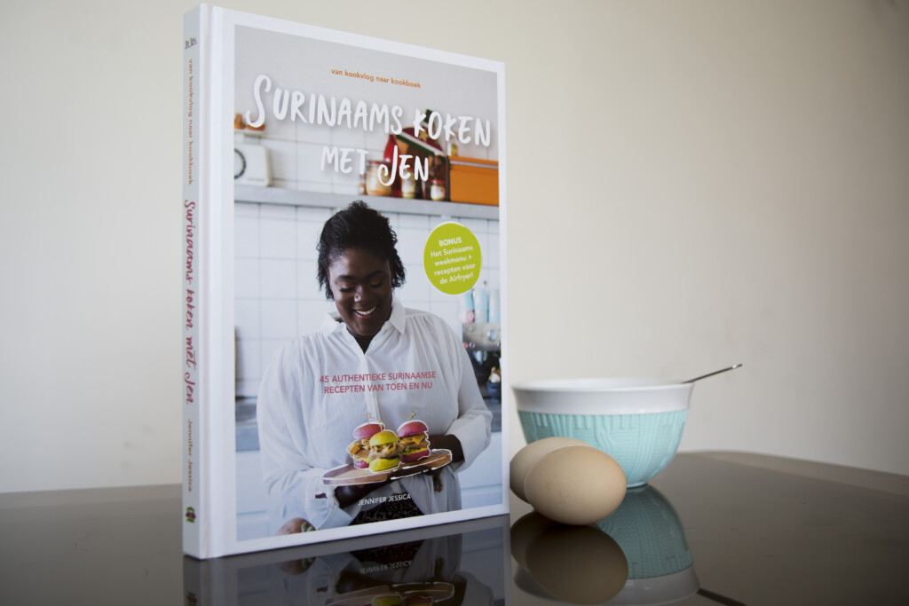 Hardcover cookbook with white cover and orange accents displayed upright beside a turquoise bowl and brown egg.