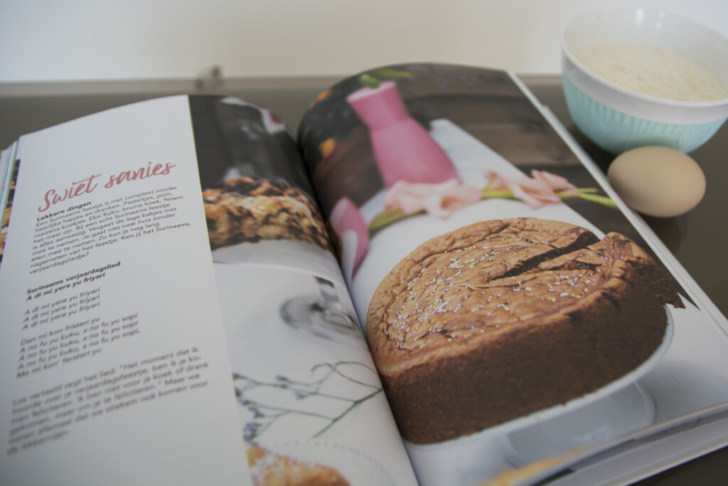 Hardcover cookbook with sewn binding displayed open showing recipe pages and food photography, accompanied by printed recipe