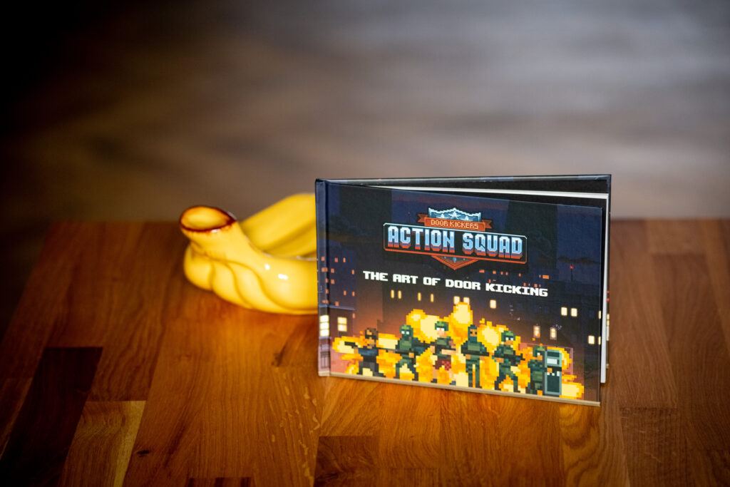 Action Squad book with yellow glowing fist design on wooden surface next to its display box showing pixel art game