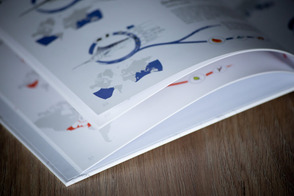 Printed catalogues fanned out on wooden surface, showing blue and red graphics on white pages with curved binding.