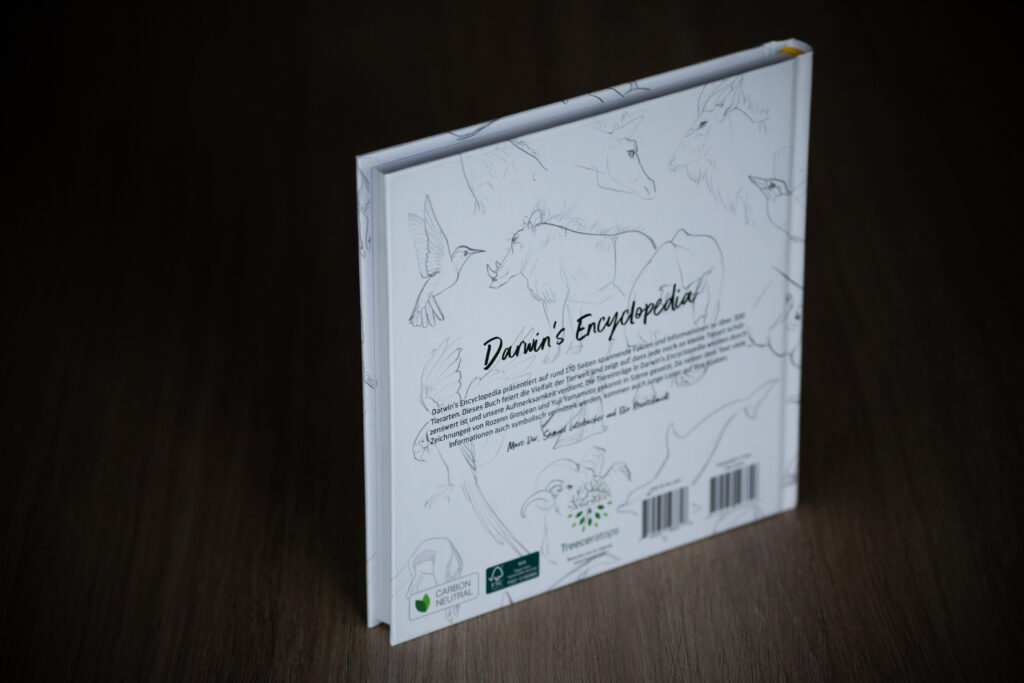 Darwin's Encyclopedia book with sketch illustrations on white cover, displayed at an angle on dark wood surface.