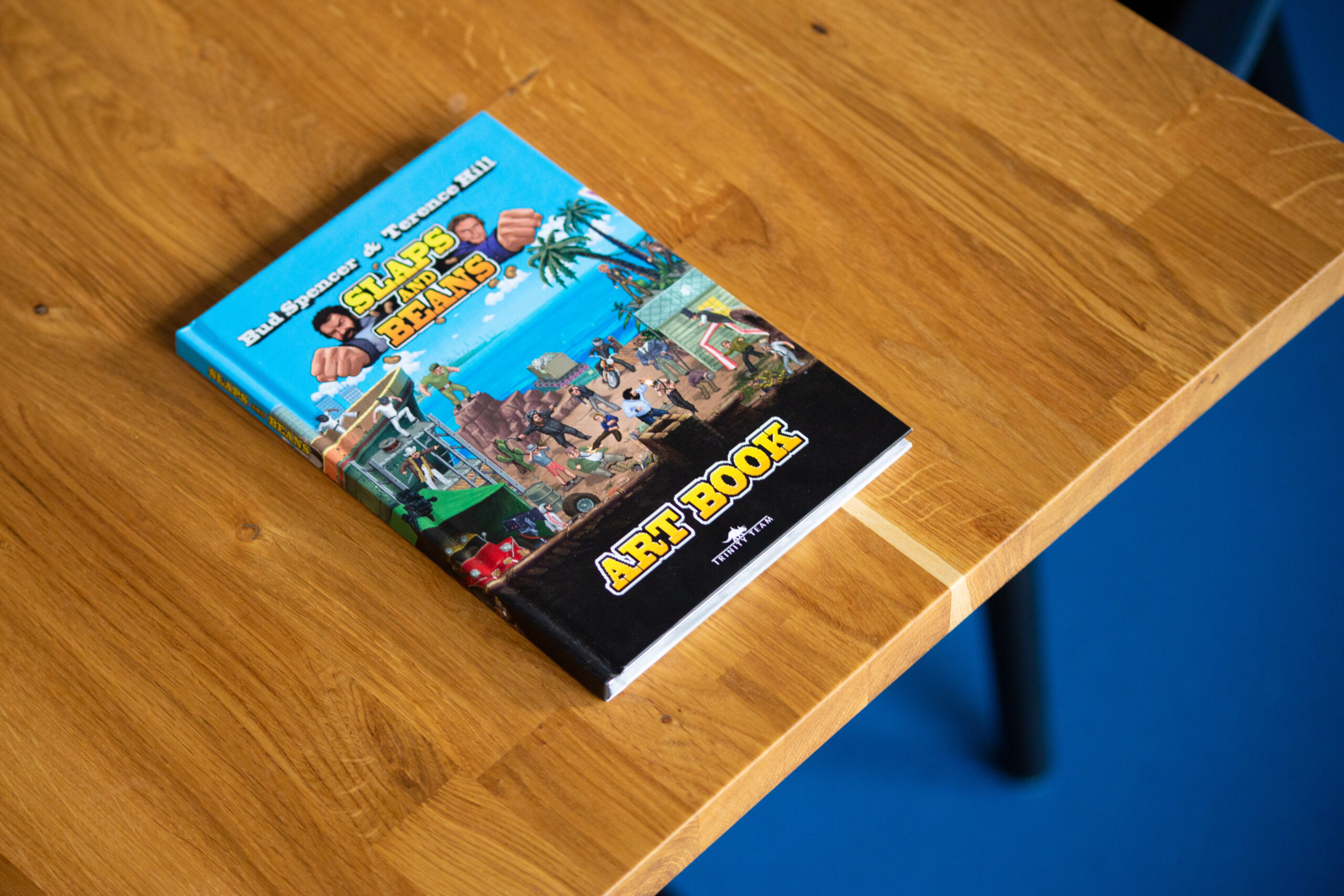 Hardcover art book with blue cover featuring colourful illustrations, displayed on wooden table.