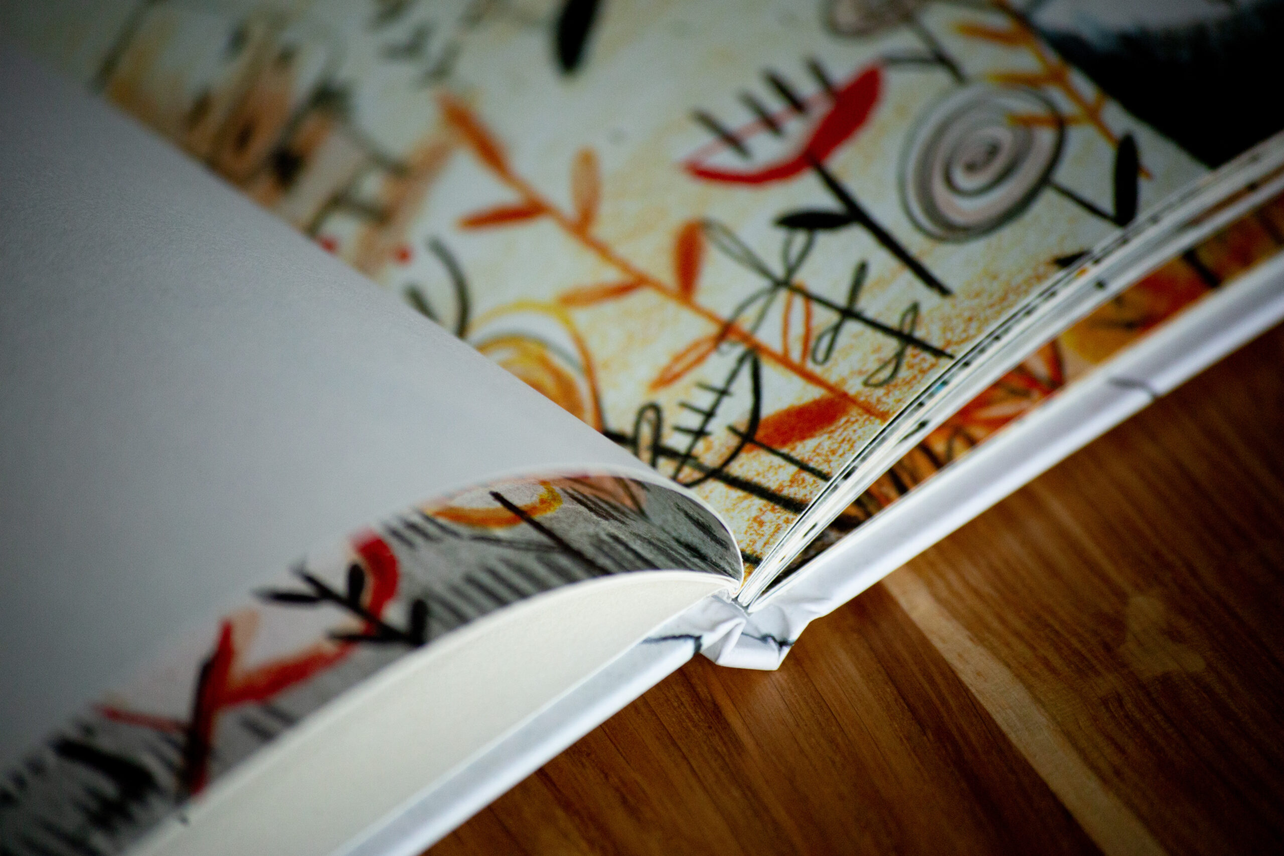 Hardcover children's book fanned open showing illustrated pages with abstract line drawings in orange, yellow, black and red