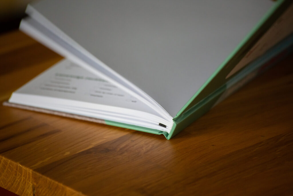 Open hardcover book with green spine on wooden surface, showing white interior pages.