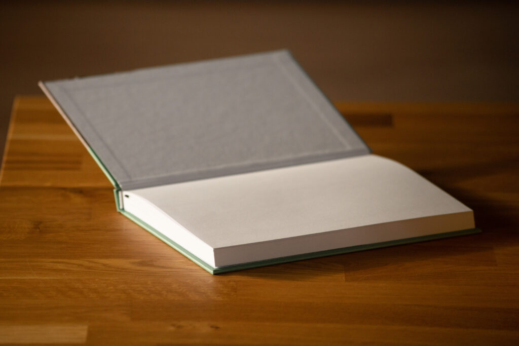 Open hardcover book with grey cloth cover and cream pages on wooden surface.