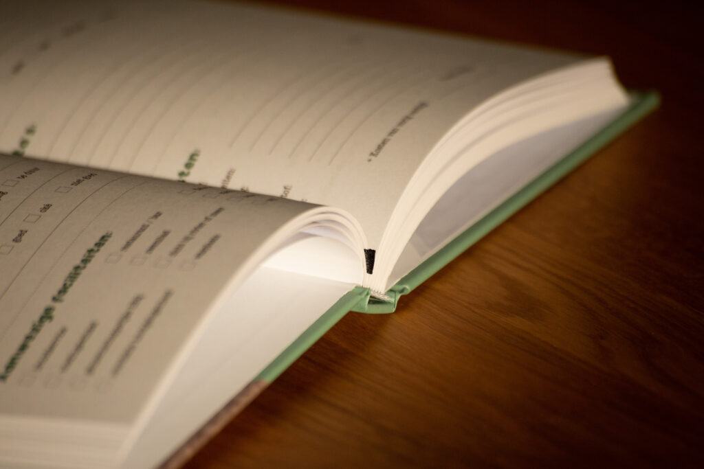 Open notebook with green spine and ruled pages on wooden surface, showing binding detail.