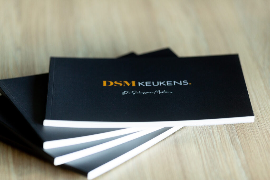 Stack of black DSM Keukens catalogues with white page edges, fanned out to show the cover and spine detail.