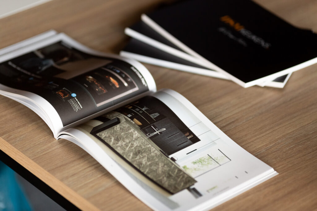 Open kitchen catalogue with gloss laminated cover featuring product photography, displayed on wooden surface with additional