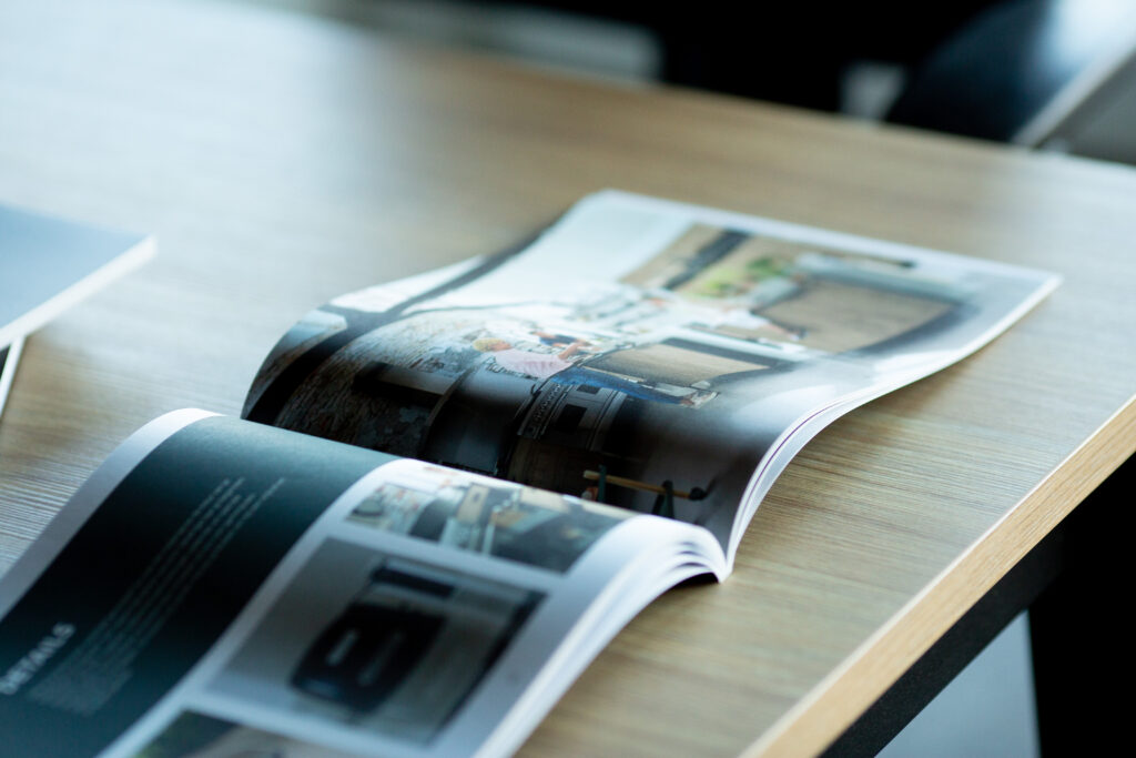 Open catalogue pages fanned out on wooden surface showing interior spreads and photography.