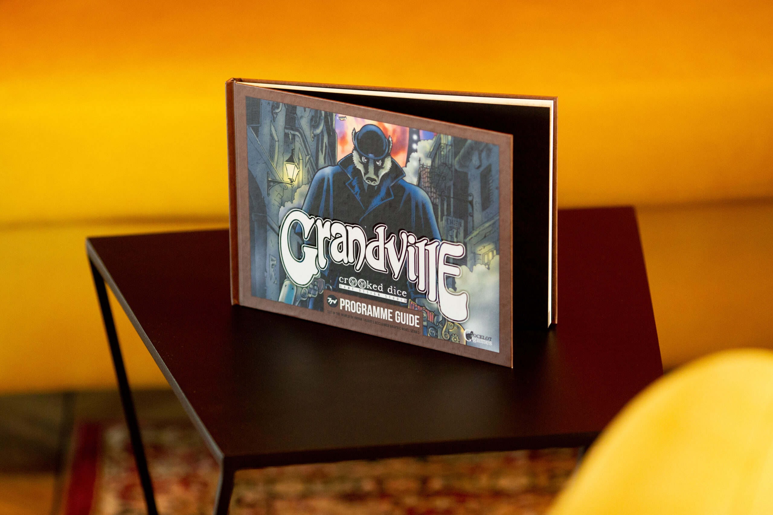 Hardcover programme guide for Grandvue with blue-toned cover featuring a figure, displayed open on a burgundy stand against